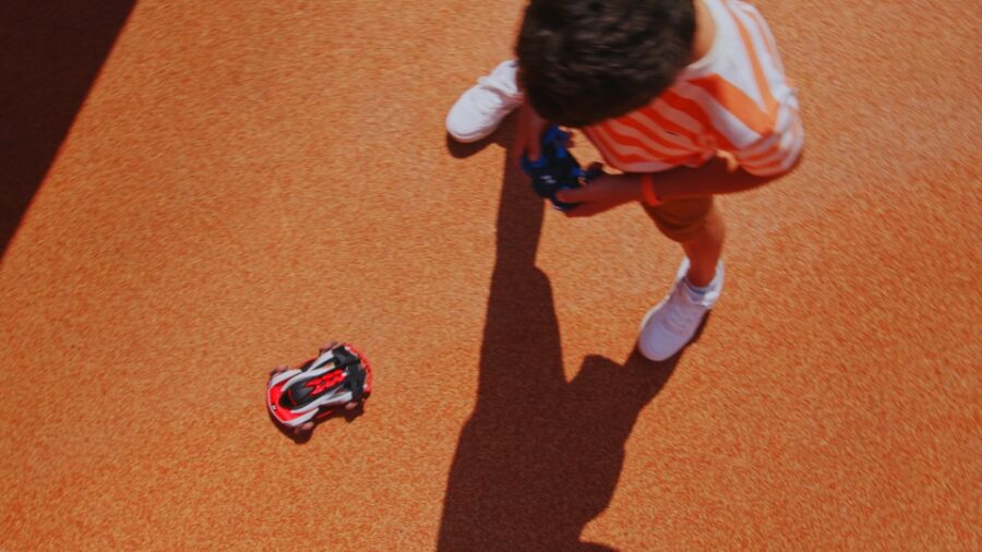 TV Advertising example - overhead shot of the boy with RC vehicle controller in hand and rc car driving between his legs on orange playground surface